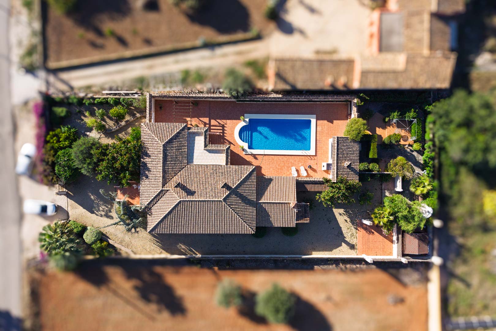Top-down aerial view of the villa on a flat plot, featuring a rectangular swimming pool, extensive paved terraces, and traditional terracotta tiled roofing.