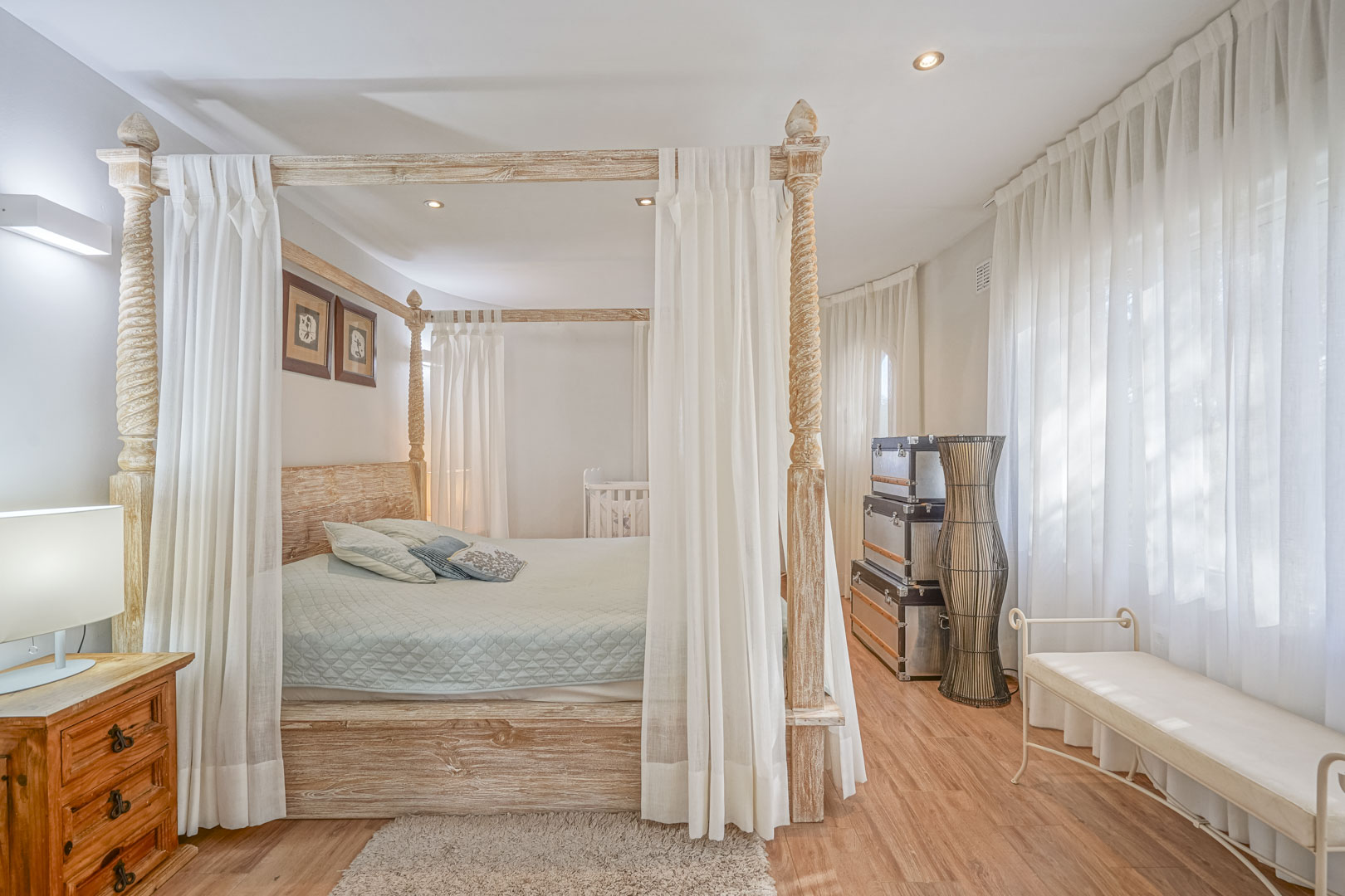 Bedroom featuring a carved wooden four-poster bed with white drapes, laminate flooring, and integrated recessed ceiling lighting.