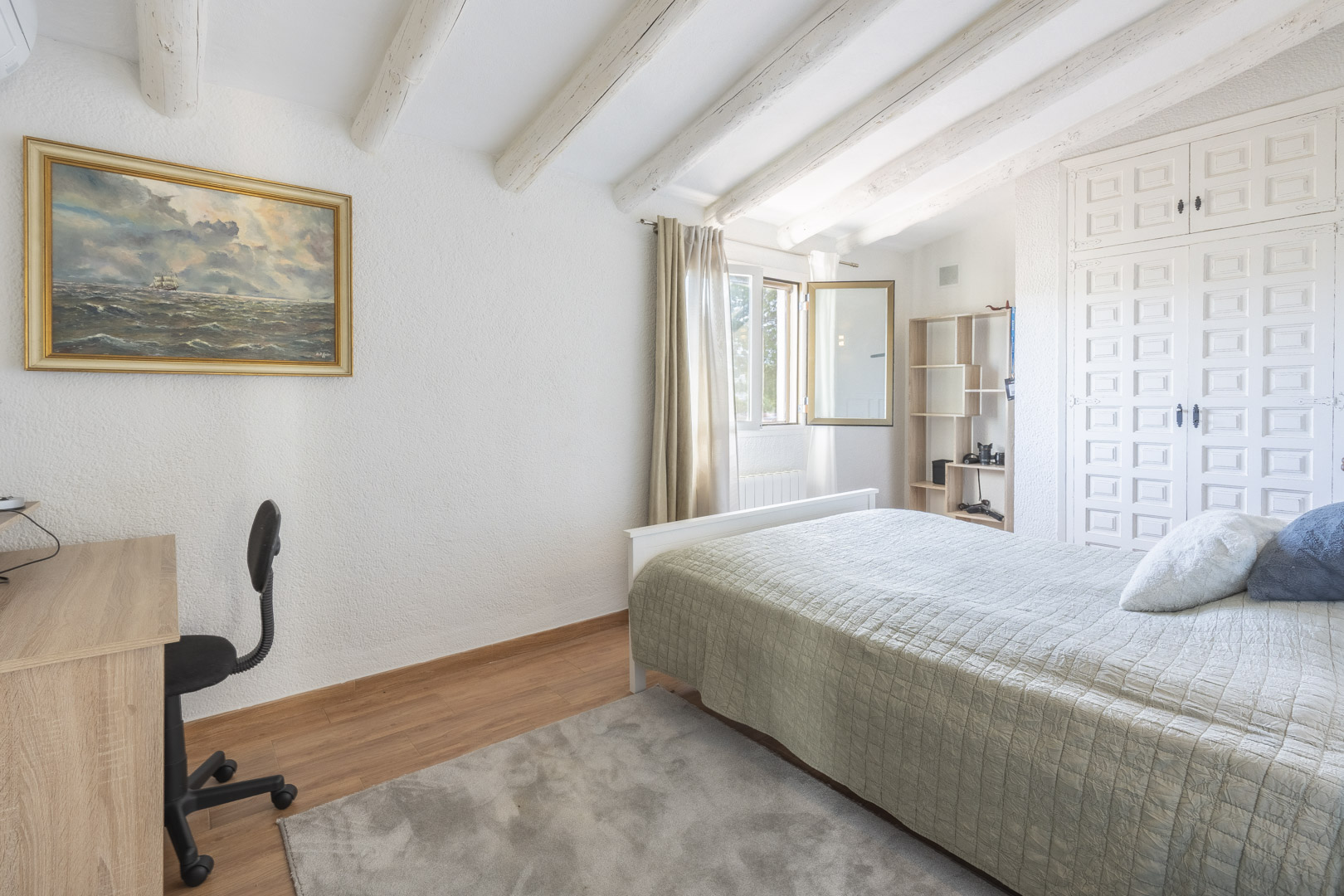 Bedroom featuring exposed white-painted wooden beams, sloped ceilings, traditional built-in wardrobes, and an integrated workspace with natural light.