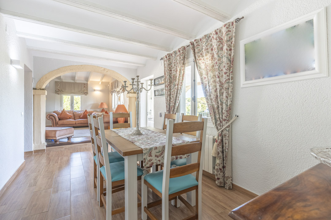 Bright dining area featuring white exposed beams and a Tosca stone archway leading to the living room. Includes wood-effect flooring and rustic furniture.