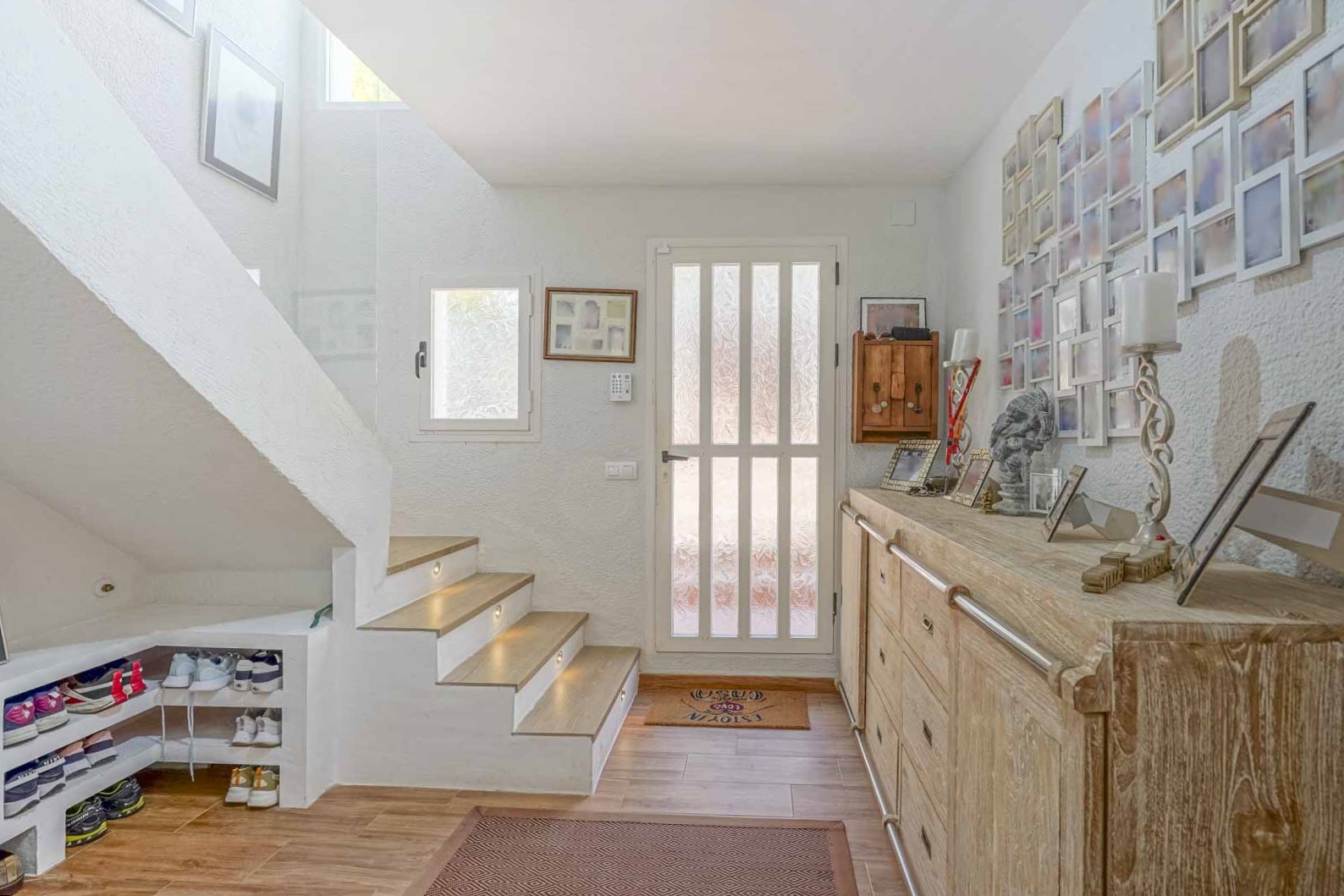 Bright entrance hall featuring a wooden staircase with integrated LED step lighting, a rustic sideboard, and custom under-stair shoe storage.