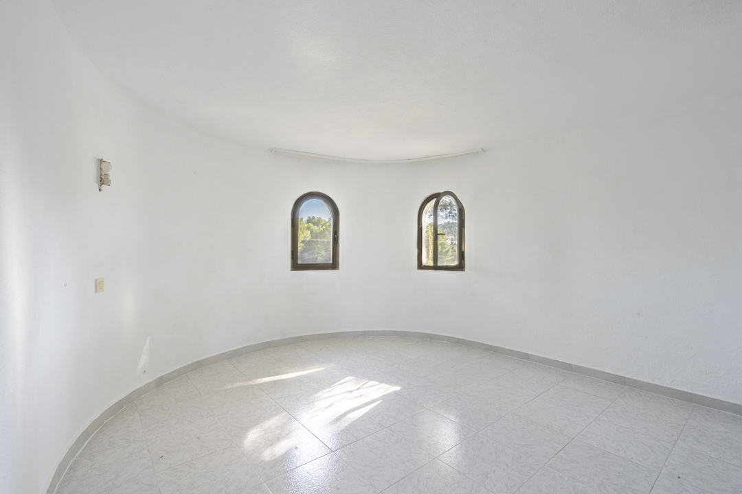 Circular room featuring white walls, light tiled flooring, and two arched windows offering natural light and views of the greenery.