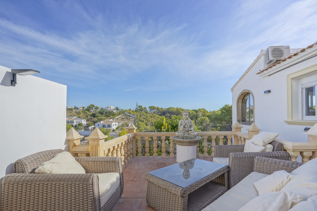 Elevated terrace featuring wicker lounge furniture, a traditional stone balustrade, and open views of the surrounding hills and Mediterranean architecture.