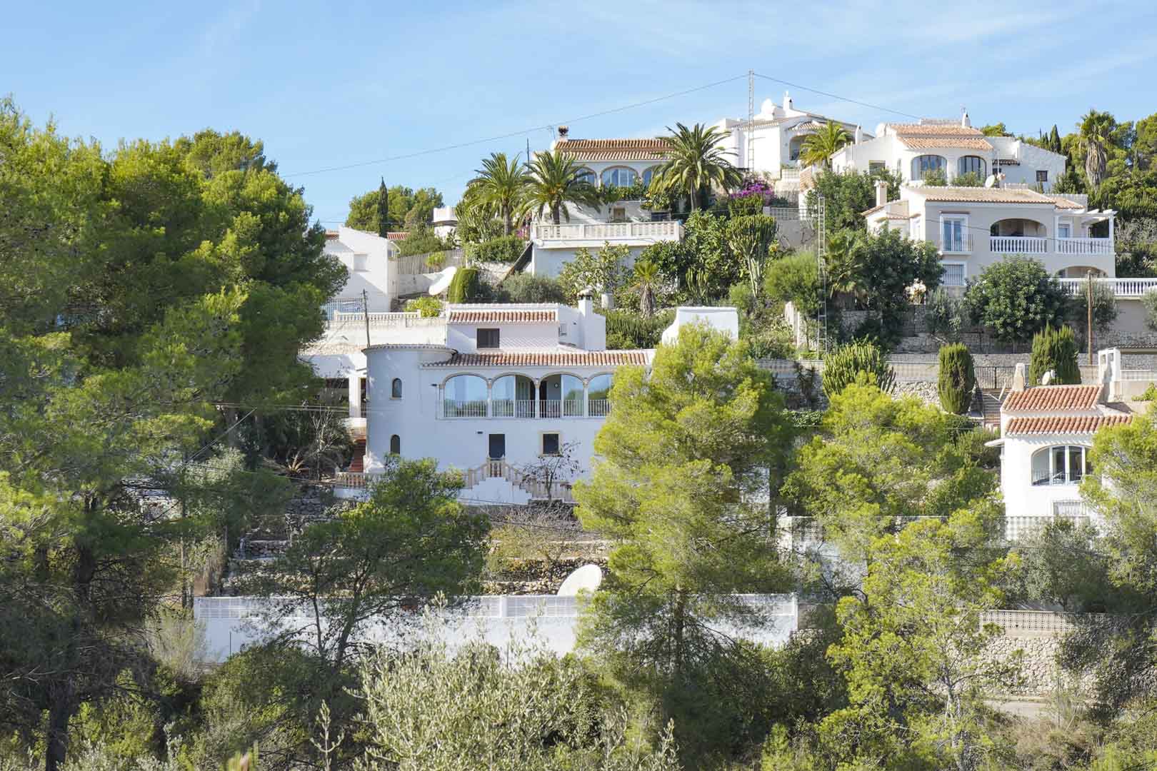 Exterior view of the Mediterranean villa set on a wooded hillside, featuring a white facade, glazed arched naya, and traditional circular tower.