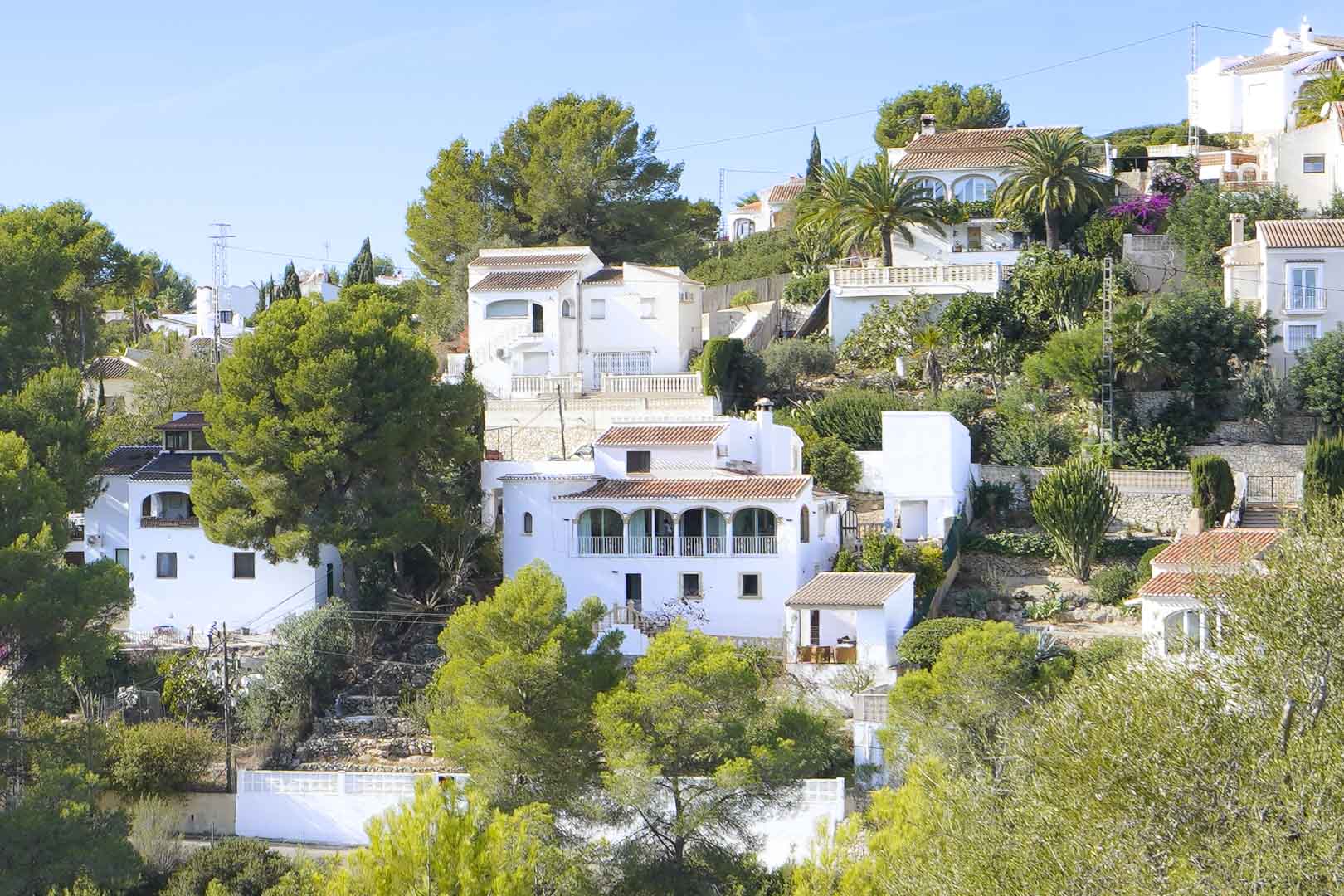Exterior view of the multi-level Mediterranean villa featuring a traditional arched naya, white facades, and terracotta roofs surrounded by lush pine trees.