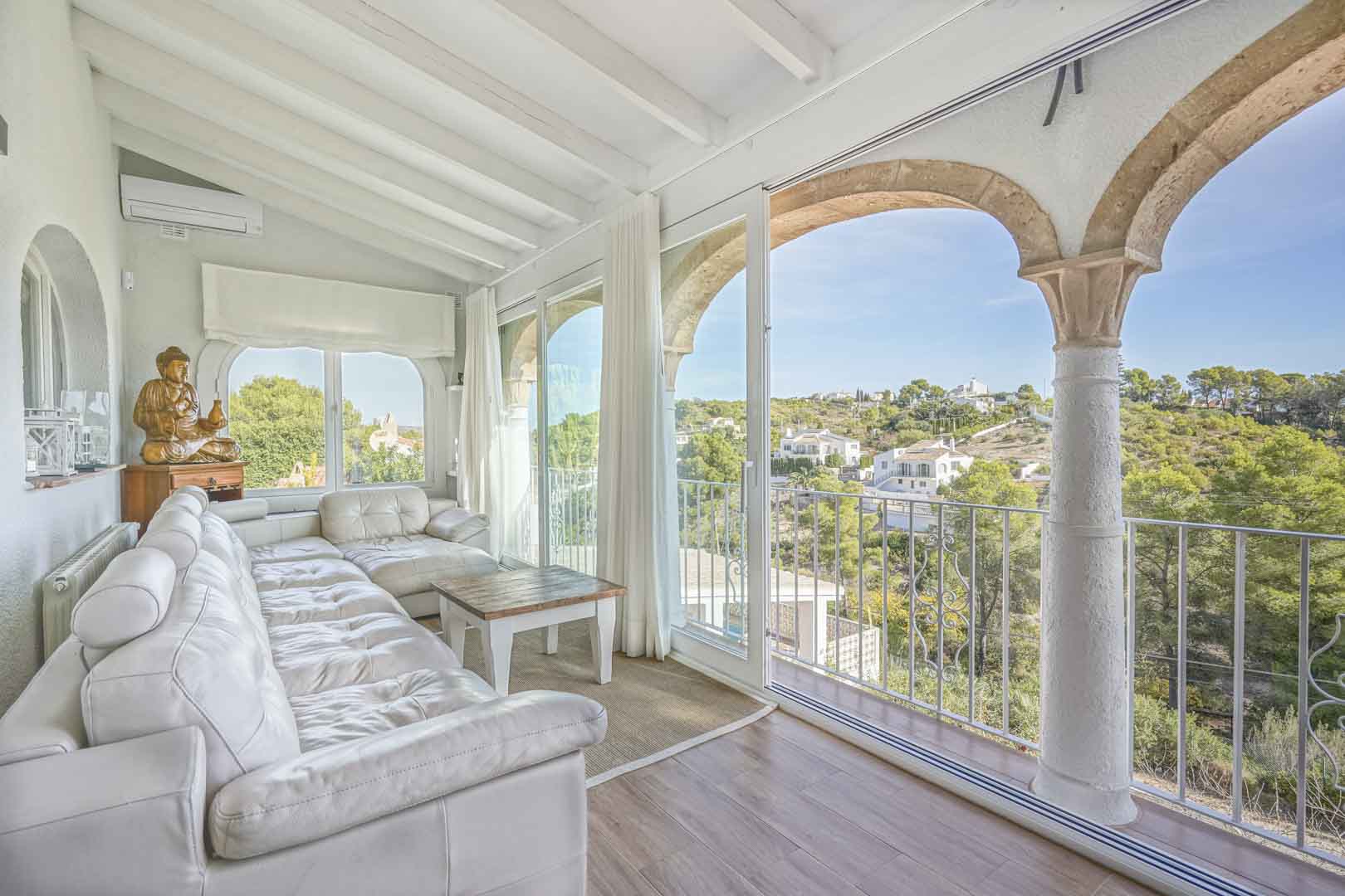 Glazed naya featuring traditional Tosca stone arches, white beamed ceilings, and panoramic valley views. Includes a large leather sofa and split air conditioning.