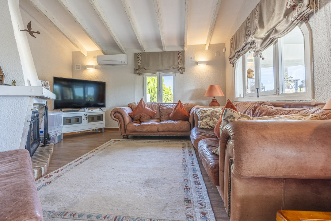 Living room featuring sloped ceilings with white wooden beams, leather sofas, a brick fireplace, and wall-mounted air conditioning.