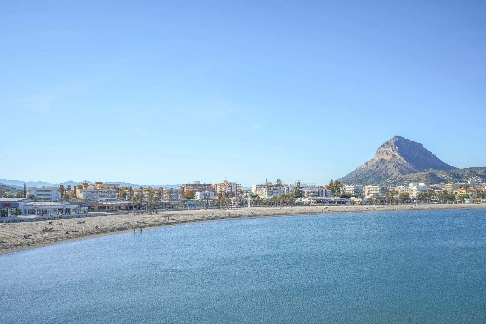 Panoramic view of Arenal Beach in Jávea, featuring the sandy bay, calm Mediterranean waters, and the Montgó mountain in the distance.