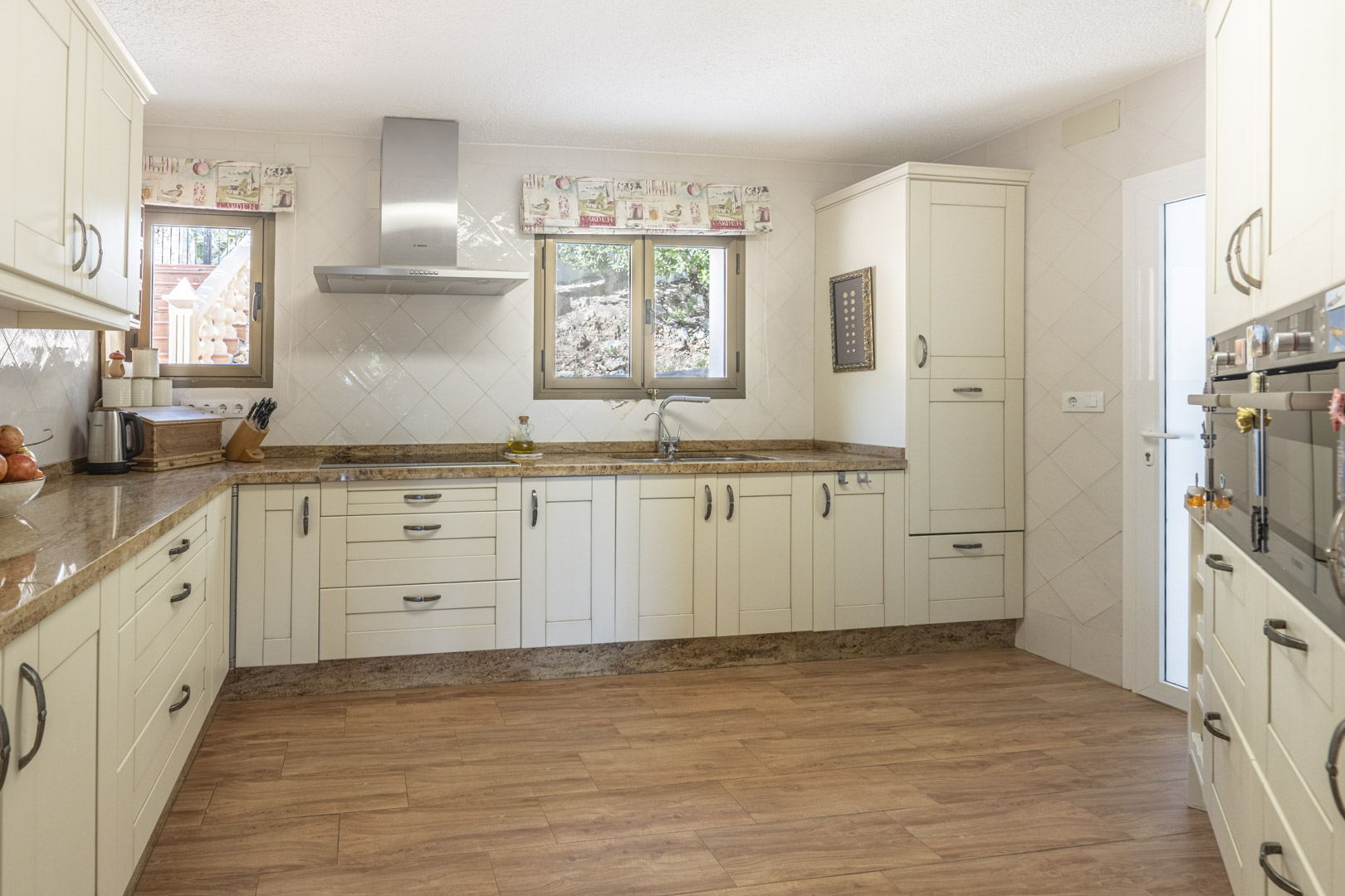 Renovated kitchen featuring cream-colored cabinetry, granite countertops, integrated appliances, and wood-effect tile flooring with natural light.