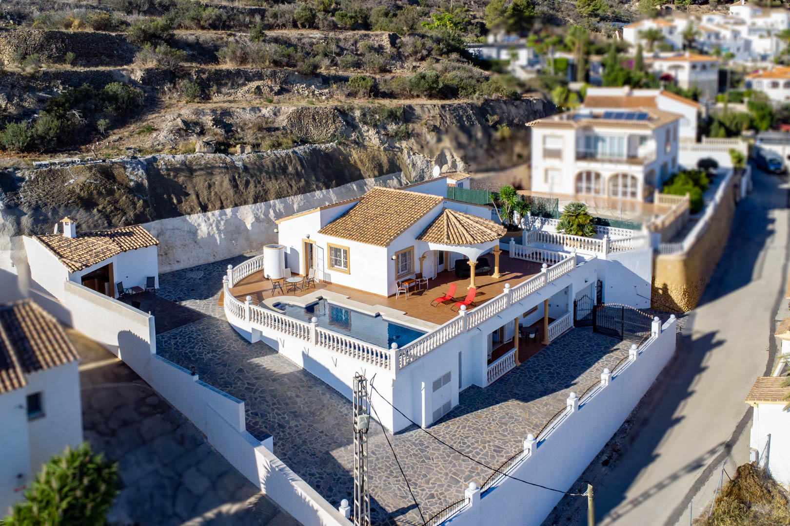 Aerial view of the villa featuring an elevated terrace with a private pool, white balustrades, terracotta roofing, and a spacious stone-paved courtyard.