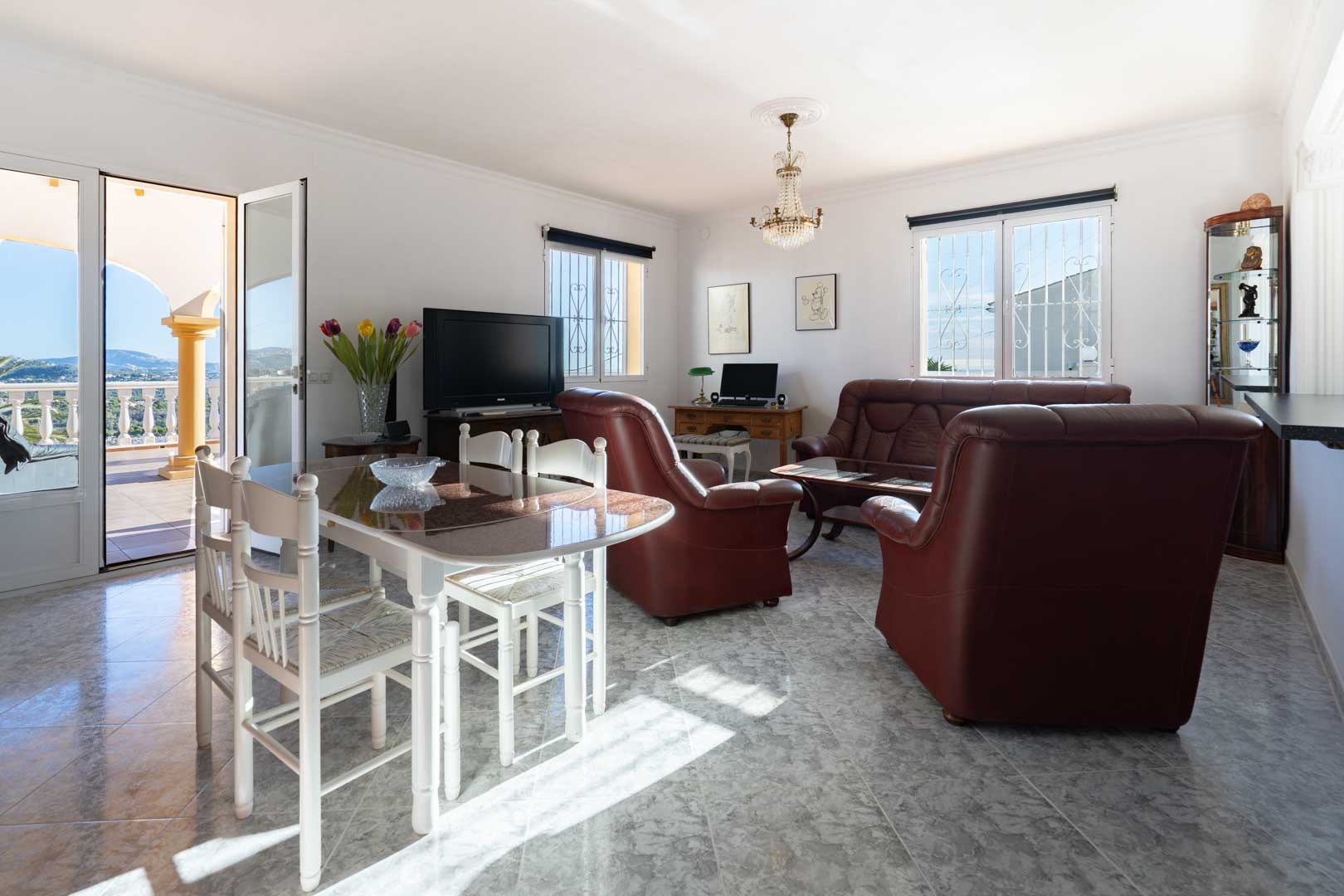 Bright living and dining area featuring marble-effect tiling, leather seating, and direct access to a terrace overlooking the Mediterranean coastline.