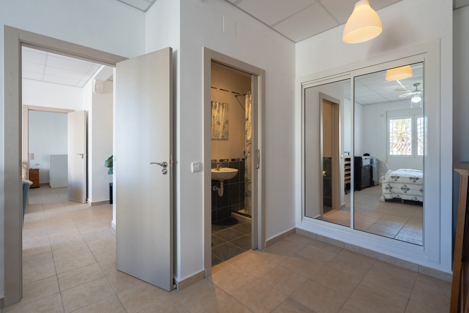 Distribution hallway featuring ceramic tile flooring, a built-in wardrobe with mirrored sliding doors, and access to a bathroom and bedroom with ceiling fan.