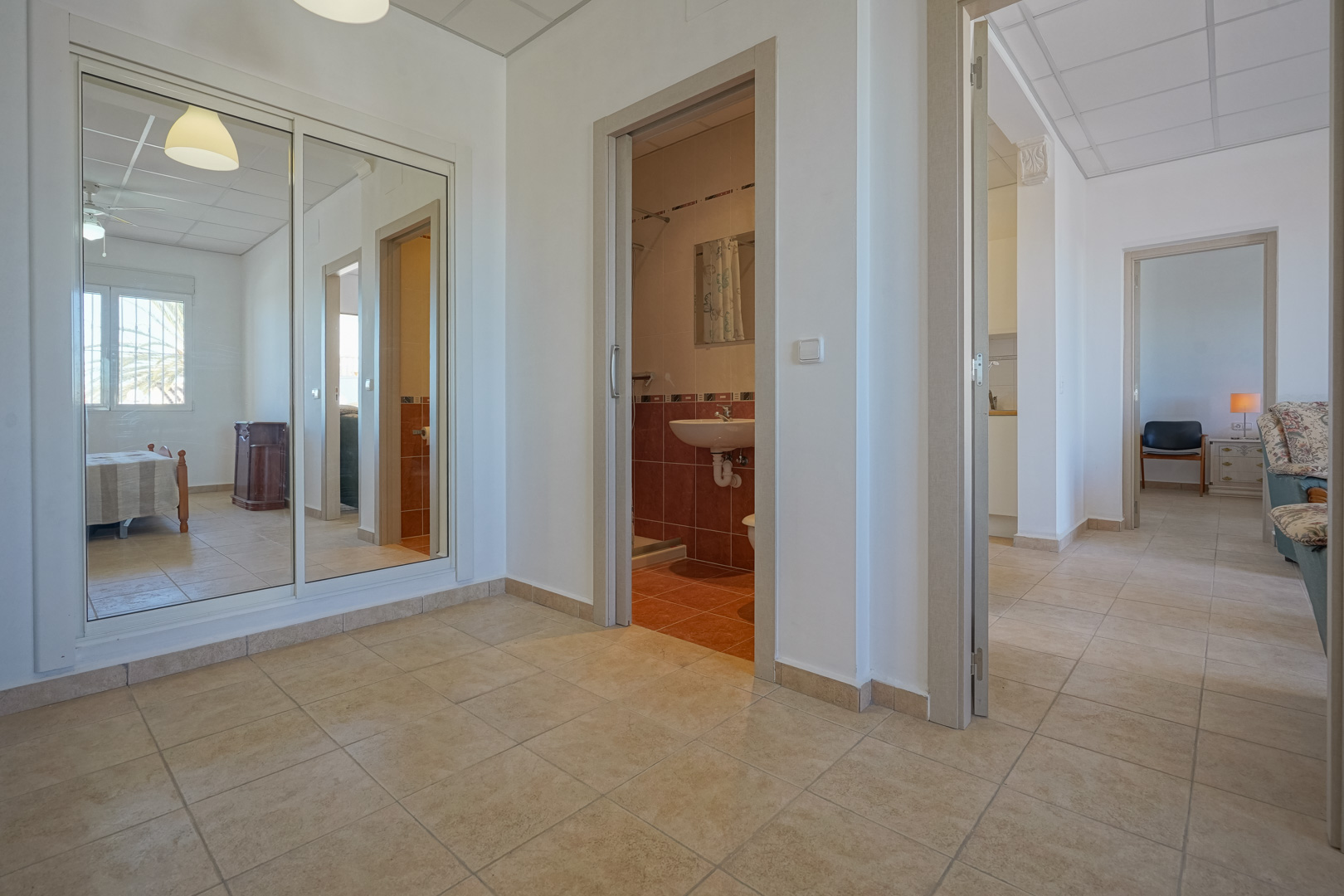 Distribution hallway featuring tiled floors, a large mirrored sliding wardrobe, and direct access to a tiled bathroom and adjacent living spaces.