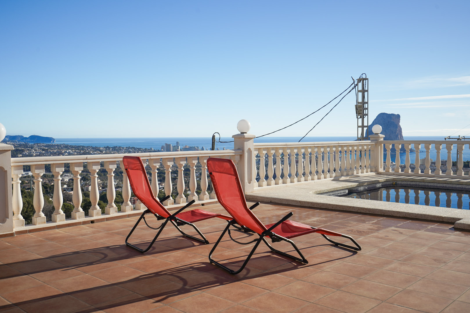 Elevated terrace featuring terracotta tiling, a classic white balustrade, and panoramic views of the Peñón de Ifach and the Mediterranean coastline.