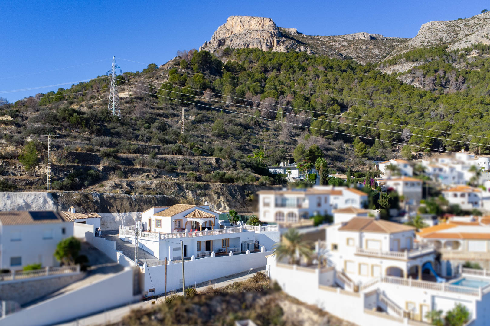 Elevated view of the white villa nestled against the Sierra de Oltà, featuring traditional Mediterranean architecture, tiled roofs, and spacious terraces.