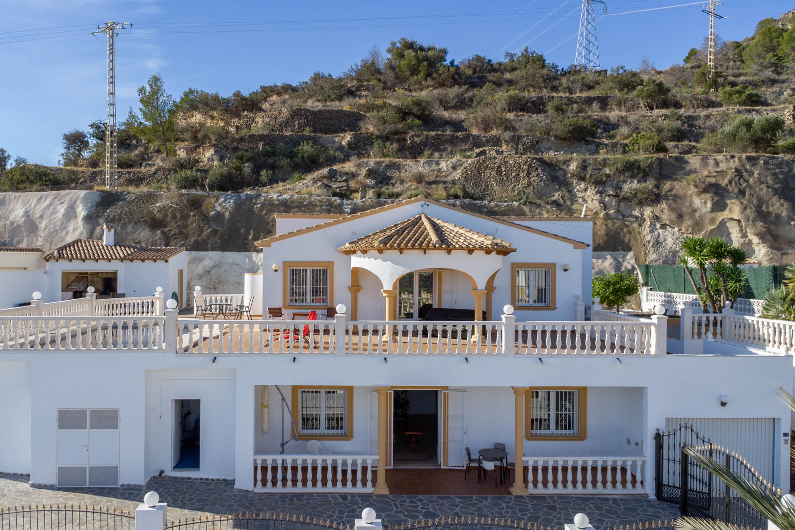Exterior view of the two-story villa featuring white facades, classic balustrades, and covered porches set against the rocky Sierra de Oltà hillside.
