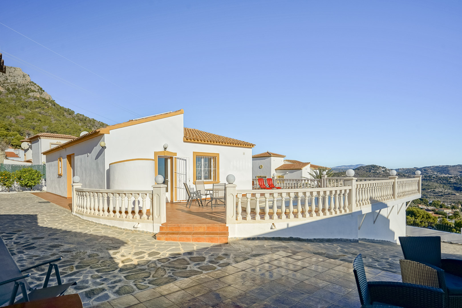 Exterior view of the villa featuring a spacious terracotta terrace with a classic balustrade, offering panoramic views of the coastline and Sierra de Oltà.