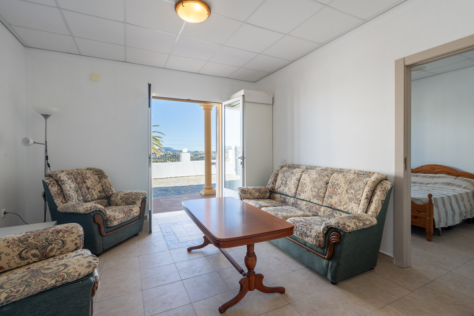 Guest apartment living room featuring floral-patterned seating, a wooden coffee table, and direct access to the terrace through a glass door.