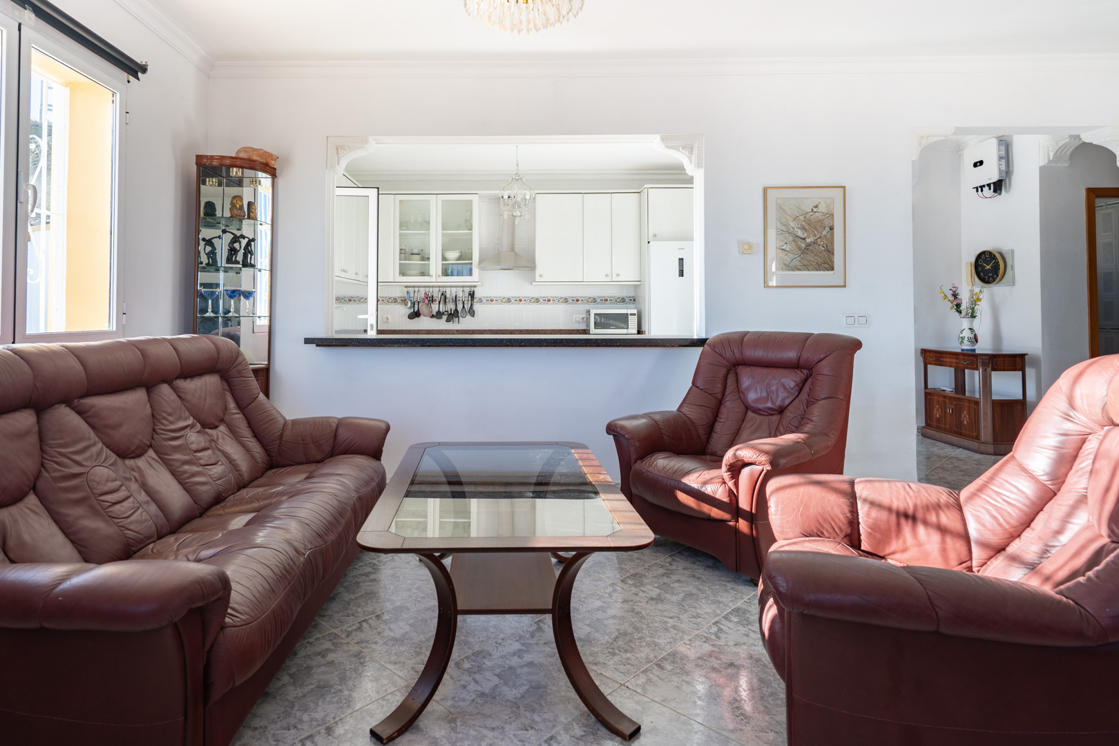 Living area featuring brown leather seating and marble-patterned tile flooring, with a pass-through opening to the semi-open kitchen.