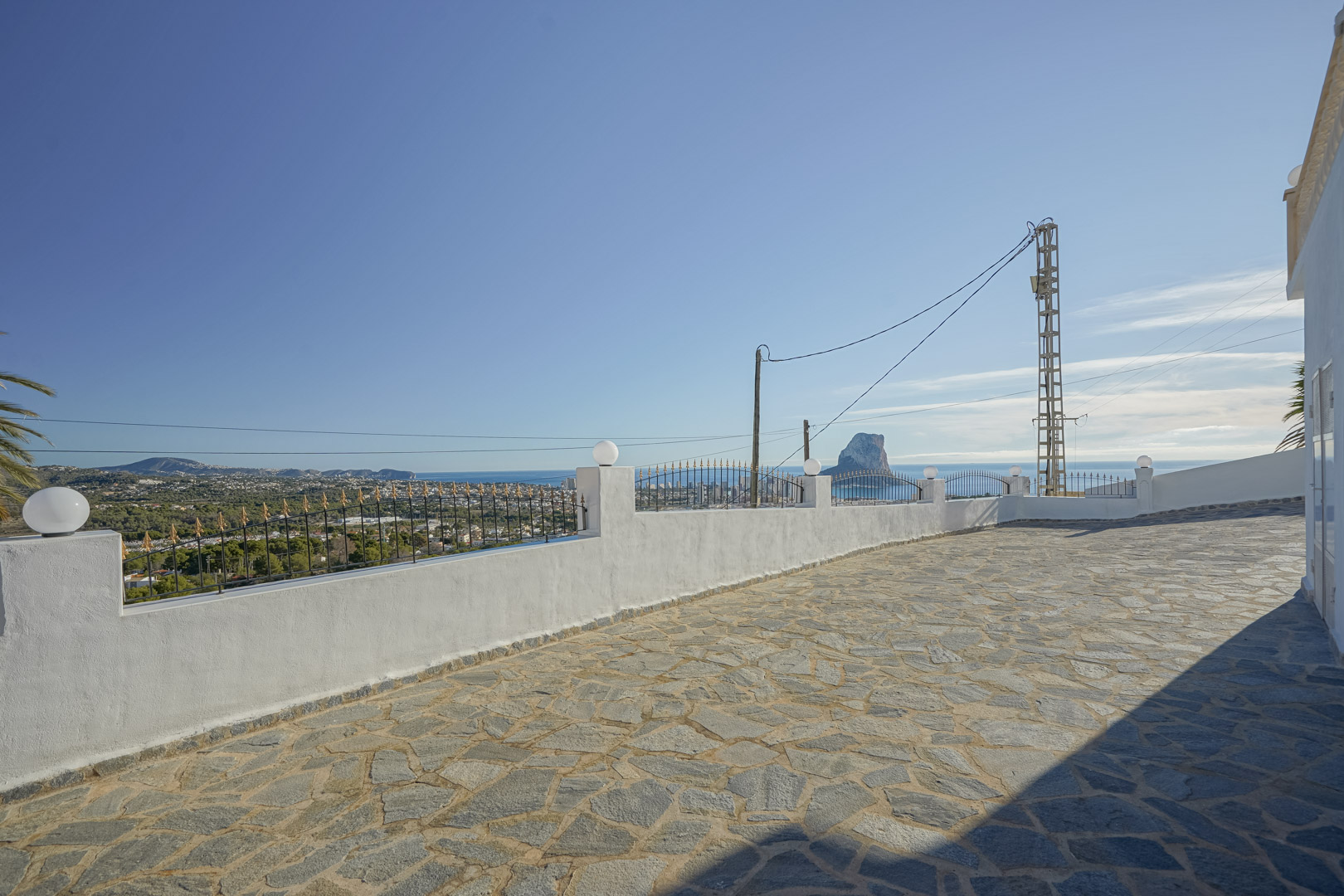 Natural stone paved terrace providing panoramic views of the Mediterranean Sea and Peñón de Ifach, bordered by a white wall with iron fencing.