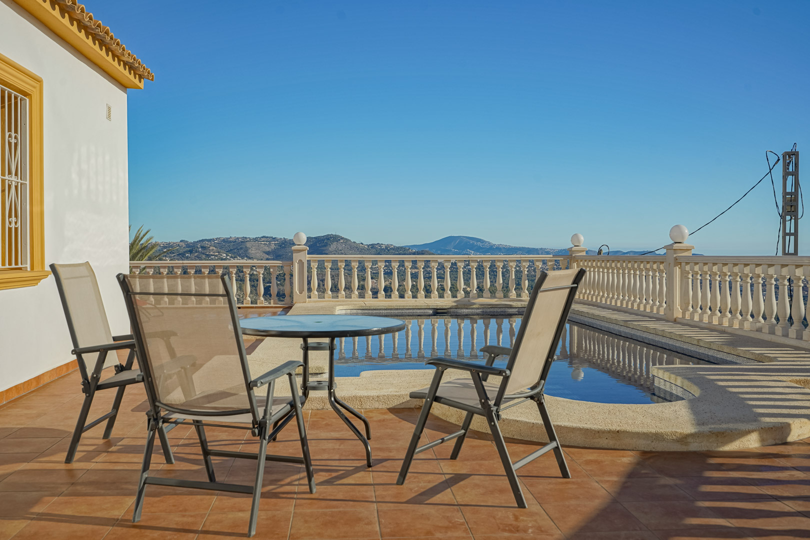Outdoor terrace featuring terracotta tiling, a glass-top table with seating, and a private pool framed by a stone balustrade with panoramic mountain views.