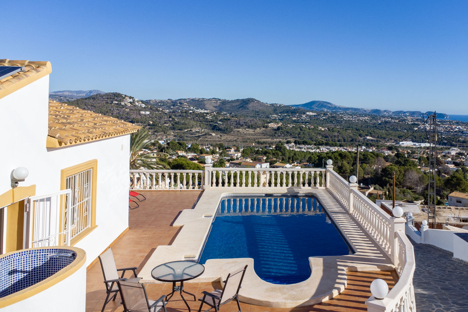 Outdoor terrace with a swimming pool, classic white balustrades, and panoramic views of the Calpe coastline and surrounding mountains.
