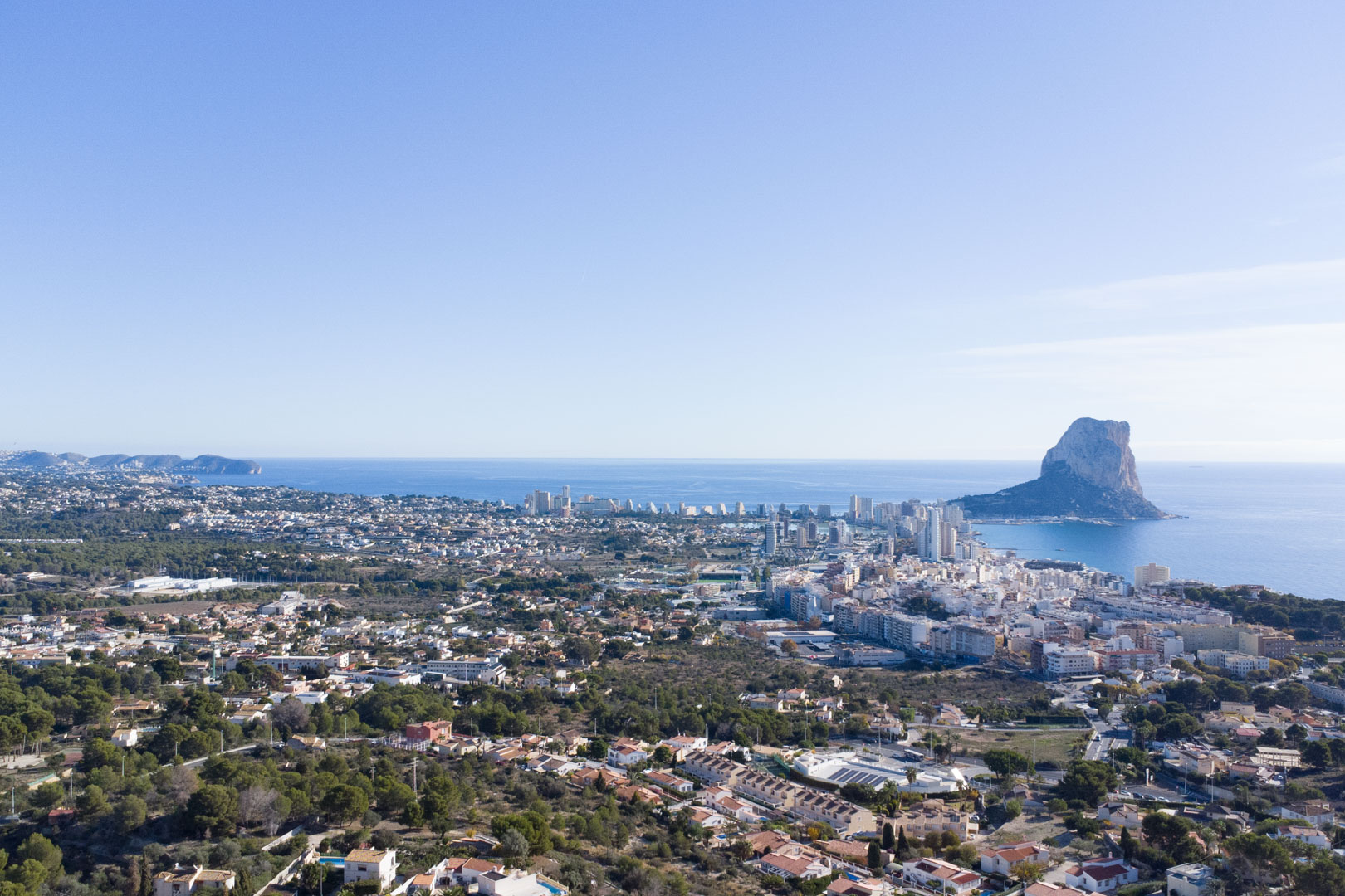 Panoramic aerial view of the Calpe coastline, featuring the Peñón de Ifach, the city skyline, and the Mediterranean Sea stretching toward the horizon.