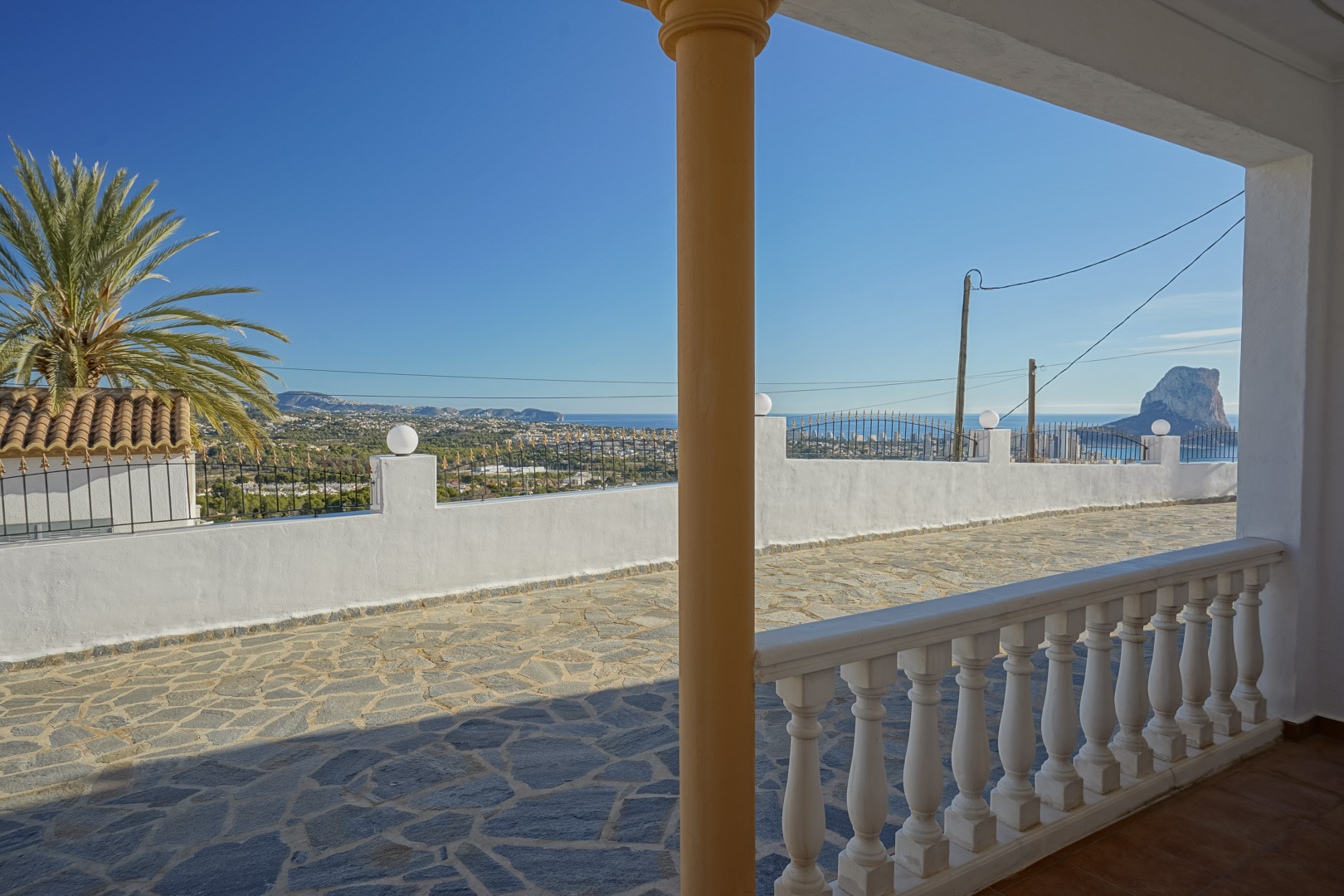 Panoramic view from the covered porch with white balustrades, overlooking the stone-paved terrace and the iconic Peñón de Ifach in Calpe.