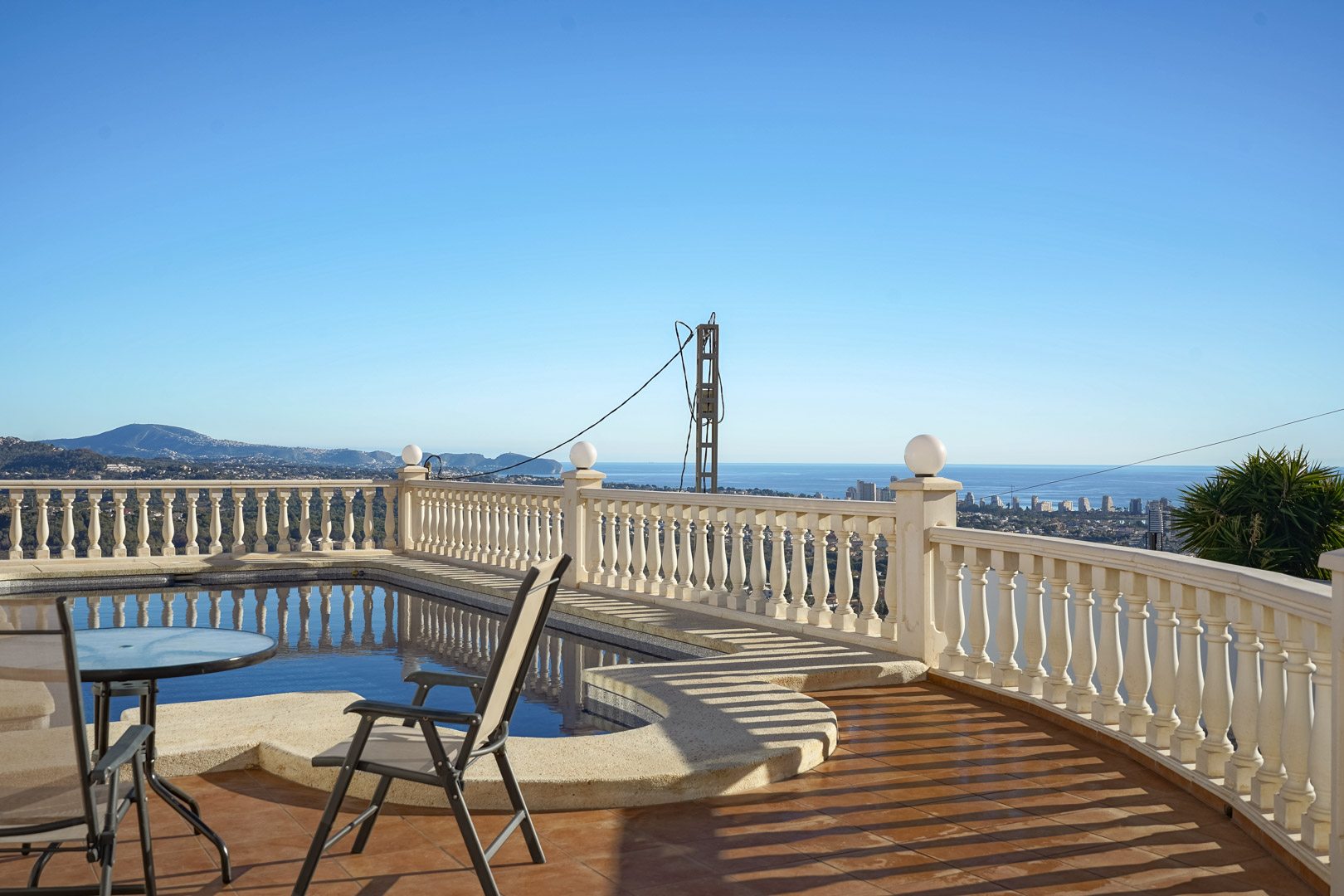 Pool terrace featuring a classic stone balustrade and terracotta tiling, overlooking the Mediterranean coastline and Calpe's skyline.