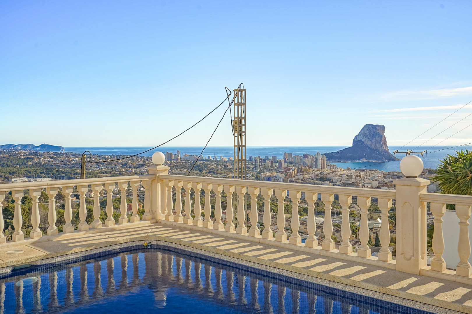 Poolside view featuring a stone balustrade and panoramic vistas of the Peñón de Ifach, Calpe's urban skyline, and the Mediterranean coast.