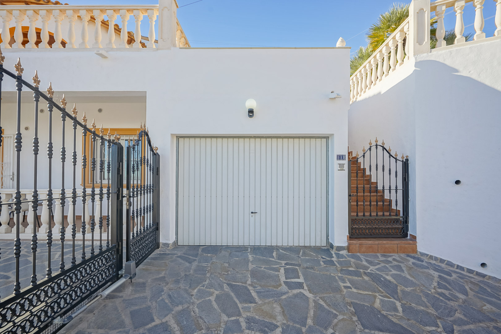 Property entrance featuring a private garage, ornate wrought-iron gates, and a stone-paved driveway leading to the exterior staircase.