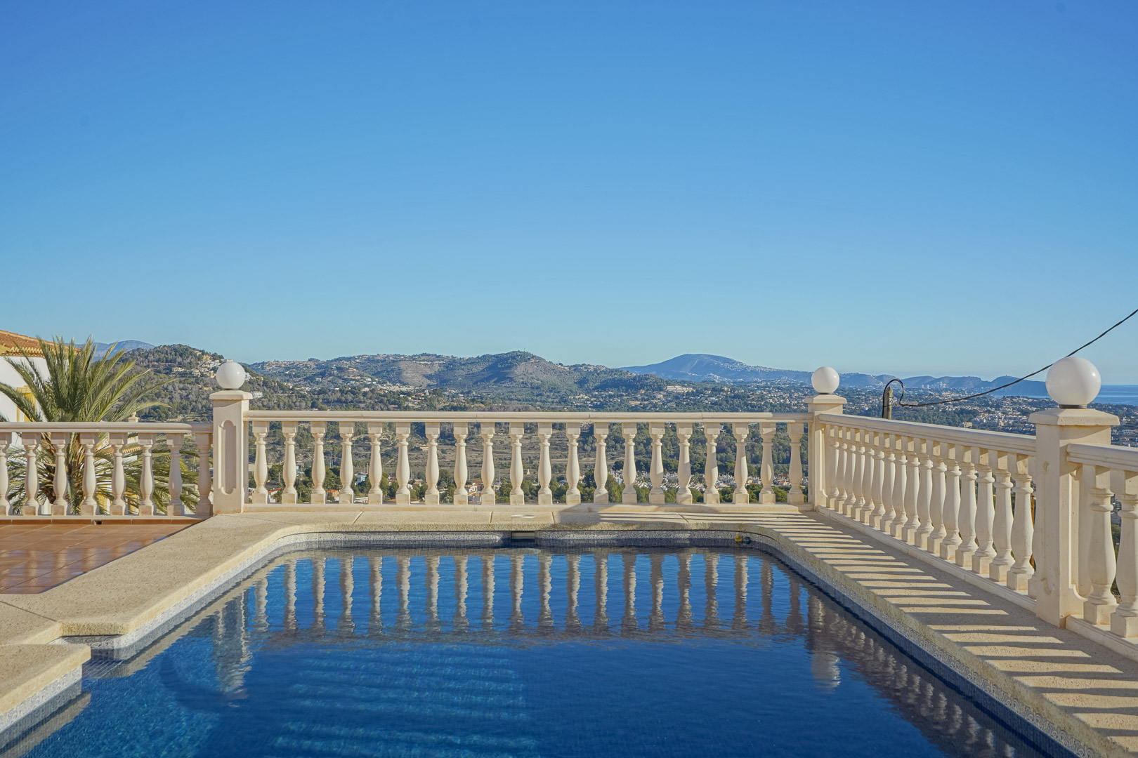 Rectangular swimming pool featuring a classic stone balustrade, offering panoramic views of the Mediterranean coastline and the mountains of the Marina Alta.