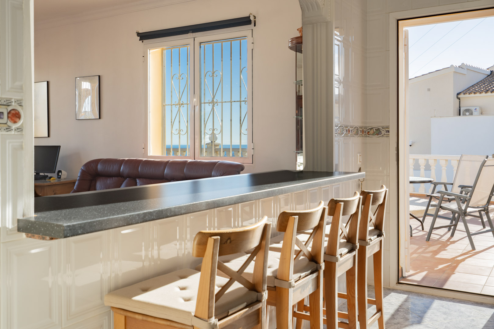 Semi-open kitchen featuring a dark breakfast bar with wooden stools, offering views of the living area and a bright terrace overlooking the Mediterranean.