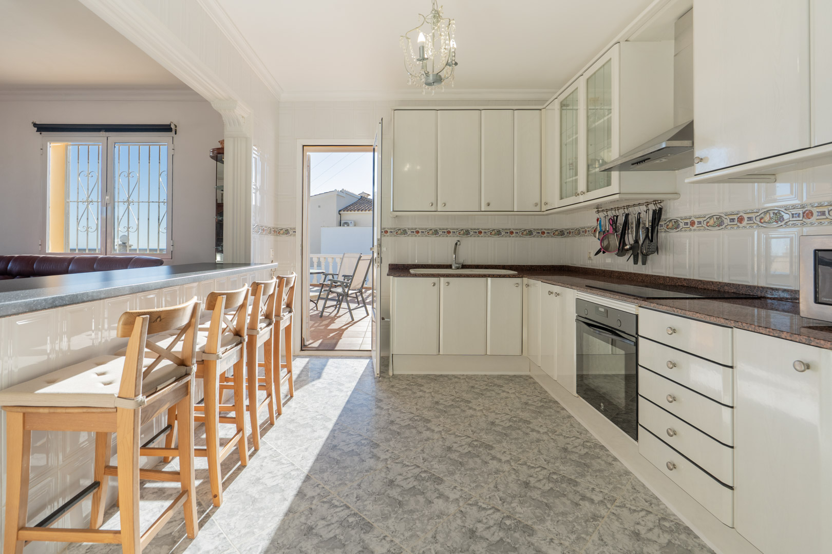 Semi-open kitchen featuring white cabinetry, granite countertops, and a breakfast bar. Includes integrated appliances and direct access to the sunny terrace.