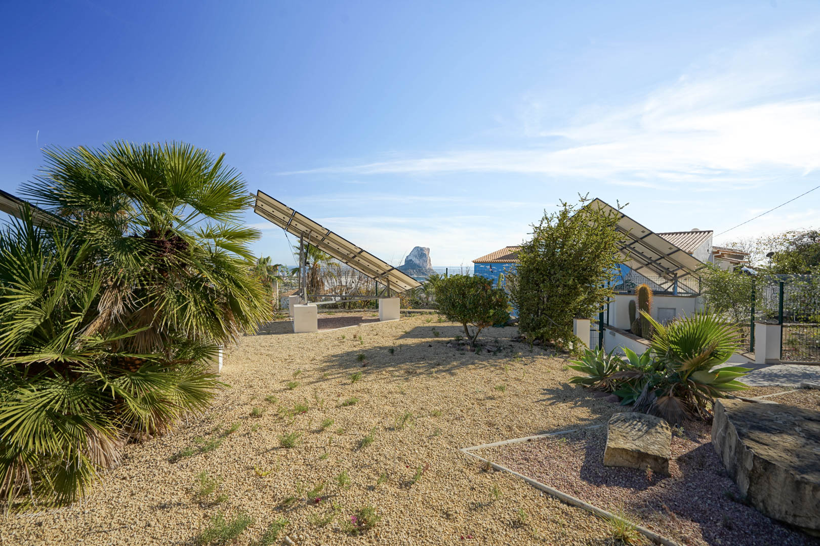 Advanced photovoltaic system featuring motorized solar towers within a gravel garden, offering clear views of the Peñón de Ifach landmark.