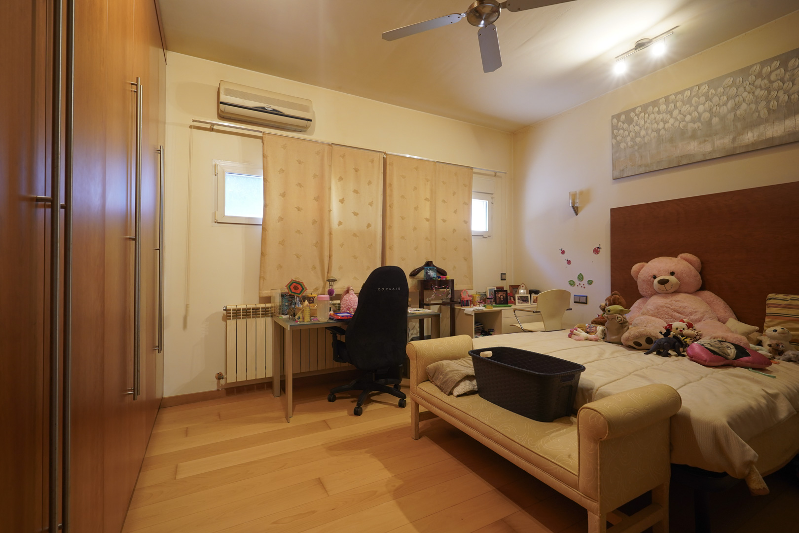 Bedroom featuring hardwood floors, spacious built-in wooden wardrobes, a dedicated desk area, split air conditioning, and a ceiling fan.