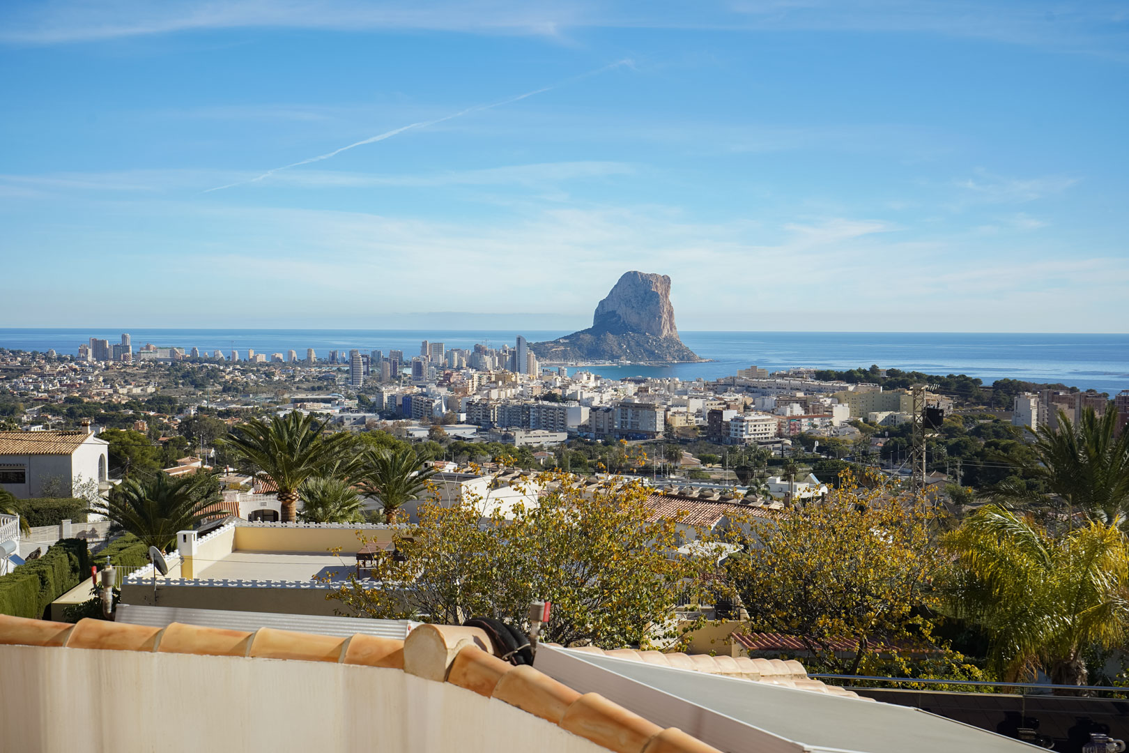 Elevated panoramic views of the Peñón de Ifach rock formation and Calpe skyline, overlooking the Mediterranean Sea and surrounding residential gardens.