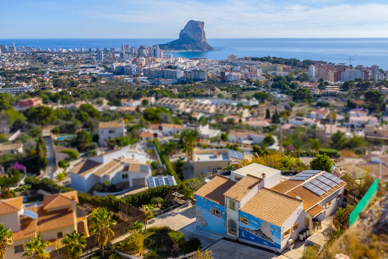 Elevated view of the villa featuring rooftop solar panels and a custom mural, overlooking the Calpe skyline and the iconic Peñón de Ifach.