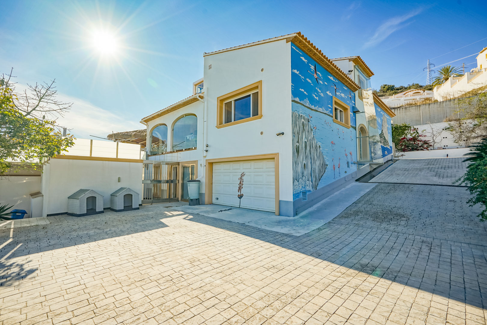 Exterior view featuring a spacious paved driveway, integrated garage, and a large custom mural of a coastal landscape on the side facade.