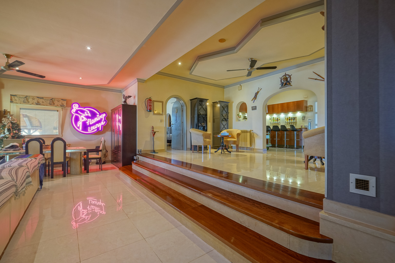 Open-plan living area featuring split-level polished tile flooring, wooden steps, and an integrated bar lounge with decorative arched entryways.