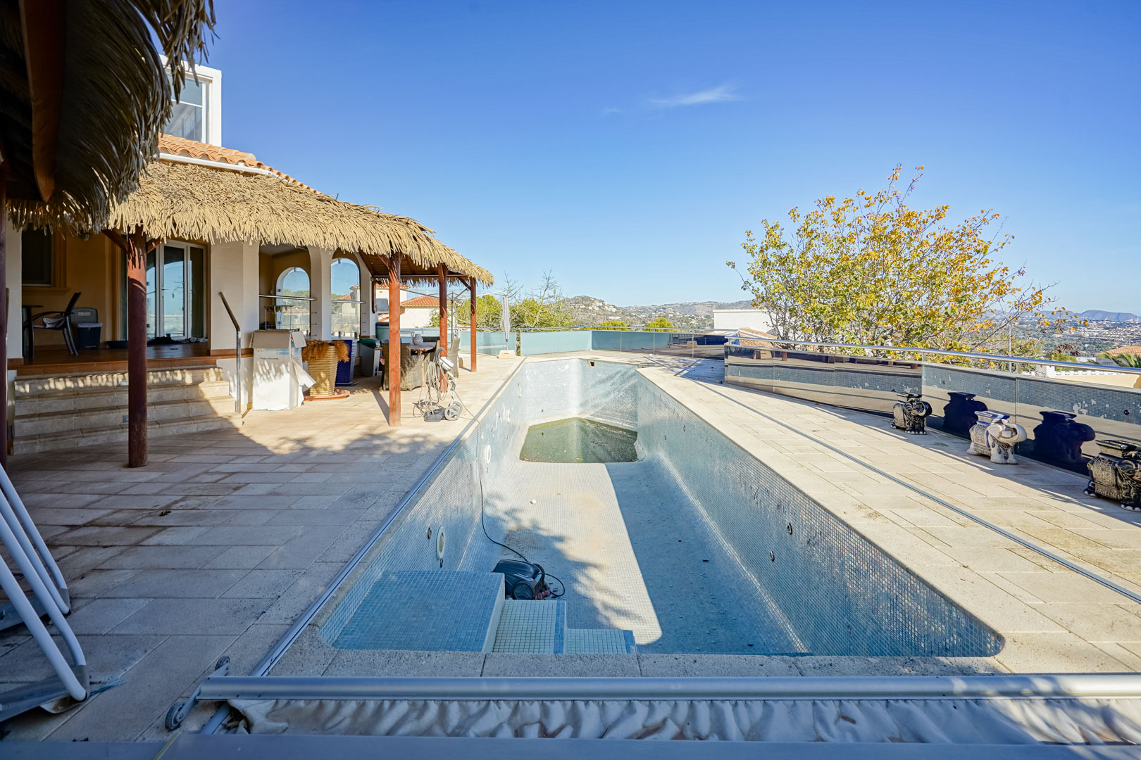 Outdoor pool area featuring a stone solarium, a rustic thatched-roof pergola, and glass balustrades overlooking the surrounding mountain landscape.