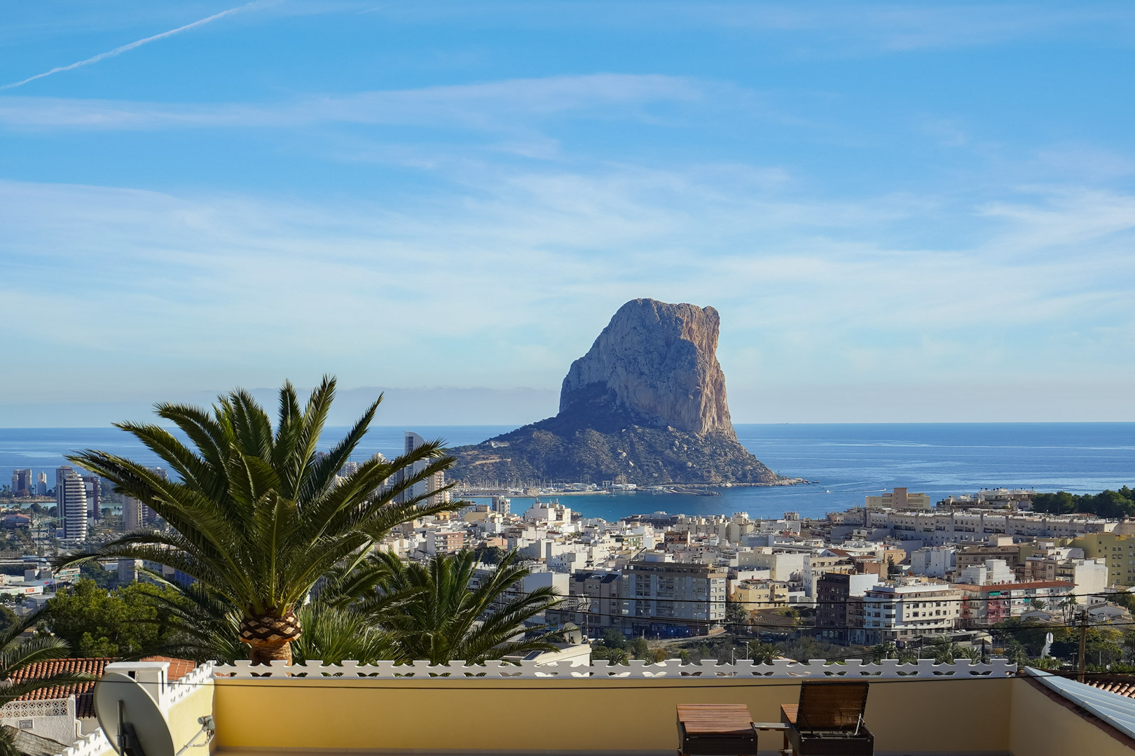 Panoramic terrace view overlooking the Peñón de Ifach and Calpe skyline, featuring the Mediterranean Sea and lounge seating under a clear sky.