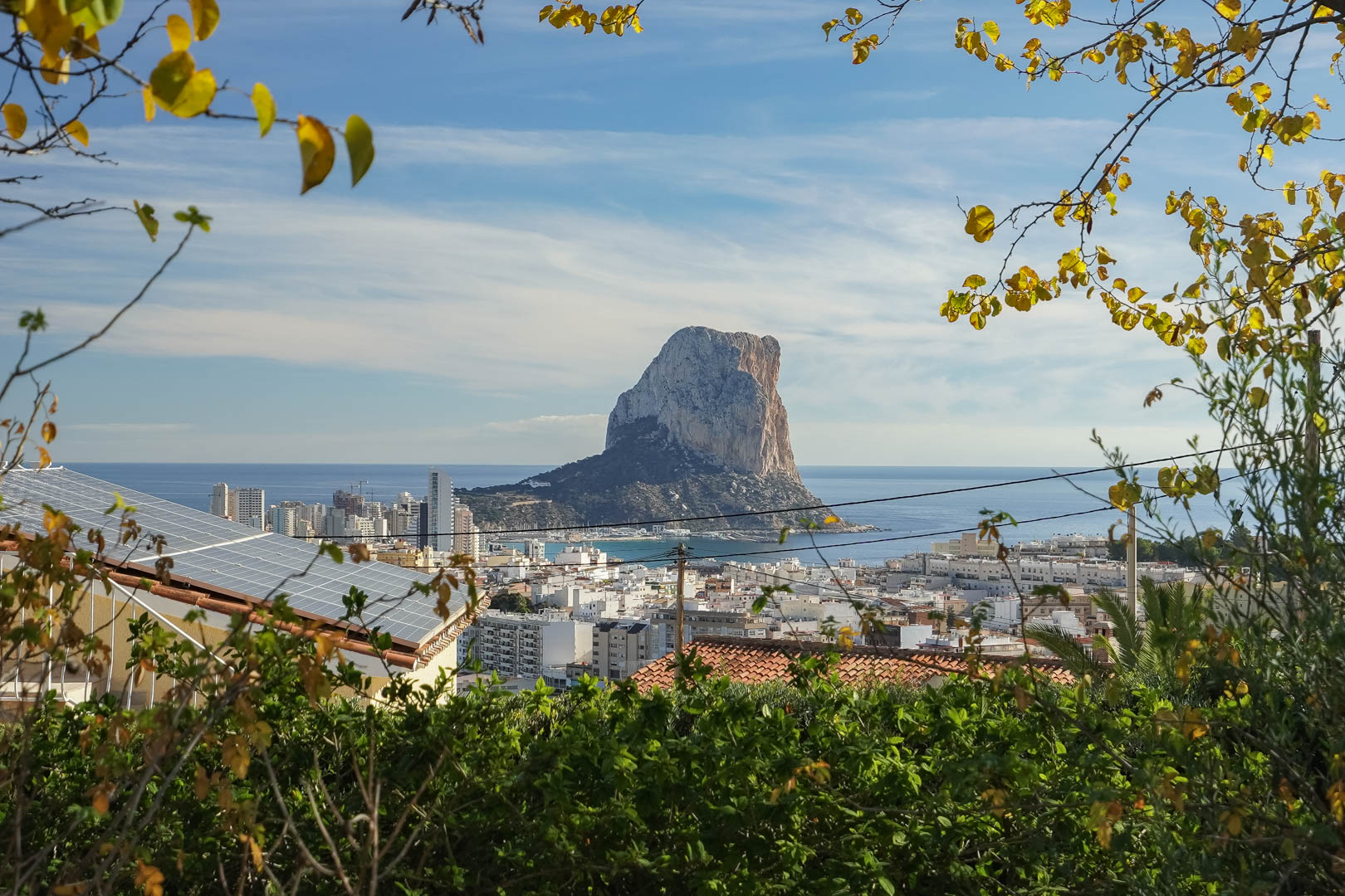 Panoramic views of the Peñón de Ifach and Calpe skyline, featuring the property's rooftop solar panel installation framed by Mediterranean greenery.