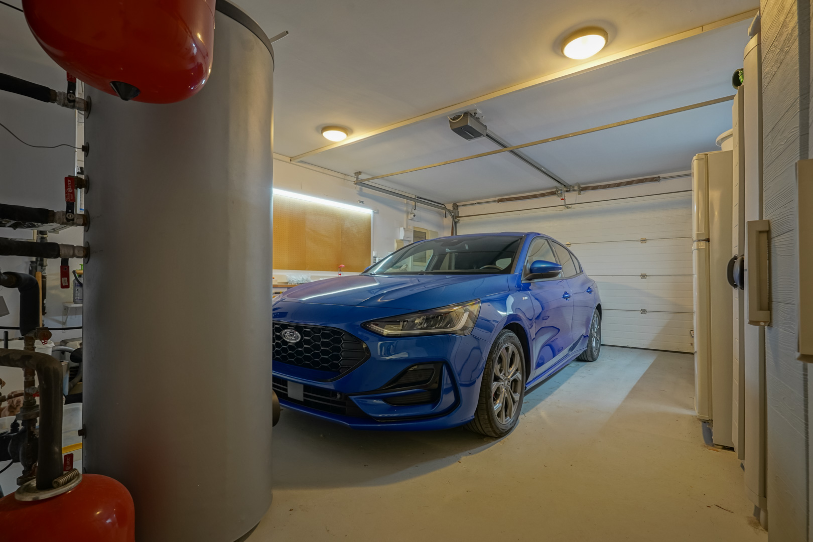 Private garage with an automatic door, a workshop area featuring LED lighting, and technical installations including a large water heater.