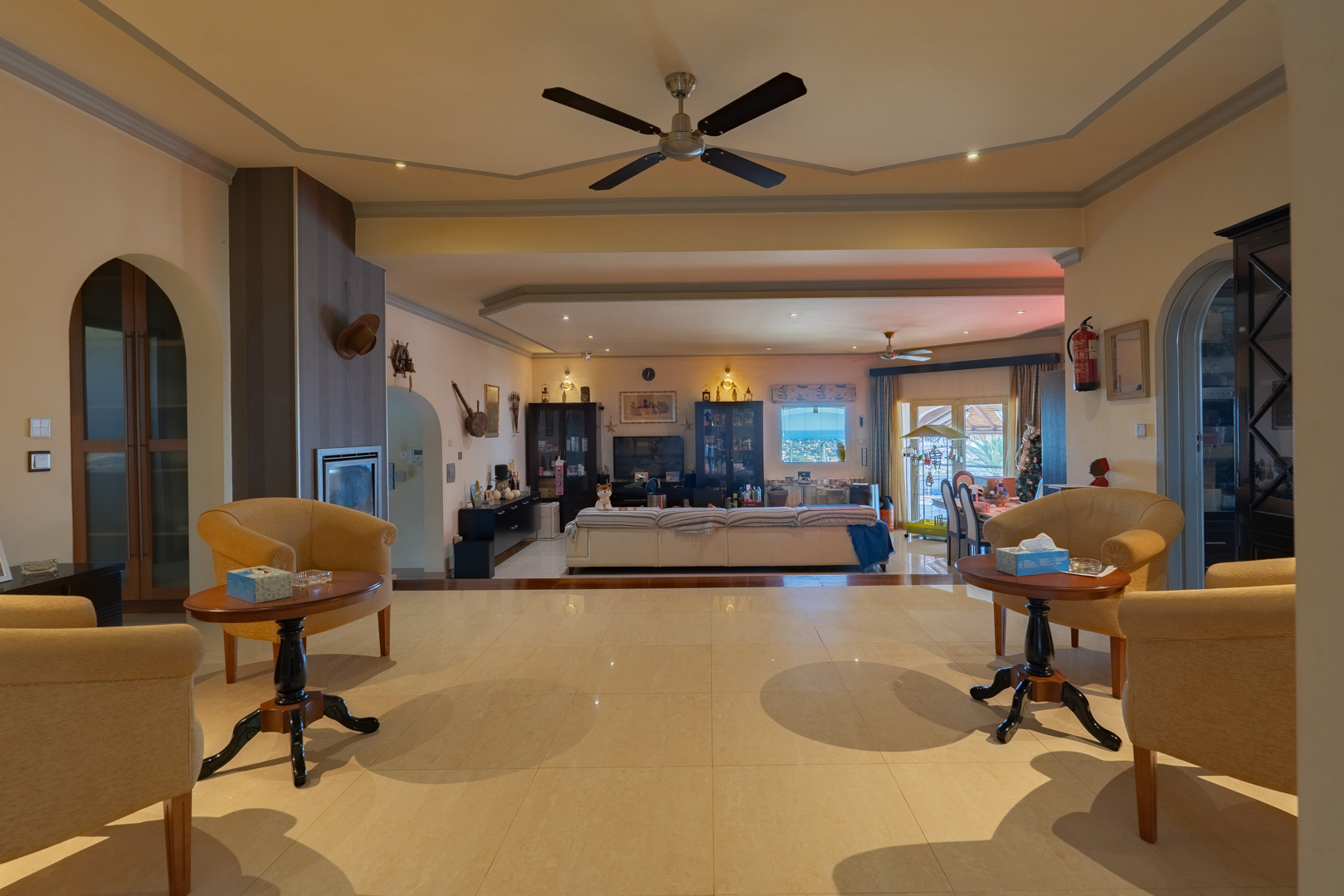 Spacious open-plan living area featuring polished tile floors, an elevated seating zone with yellow armchairs, and an integrated fireplace leading to the main lounge.