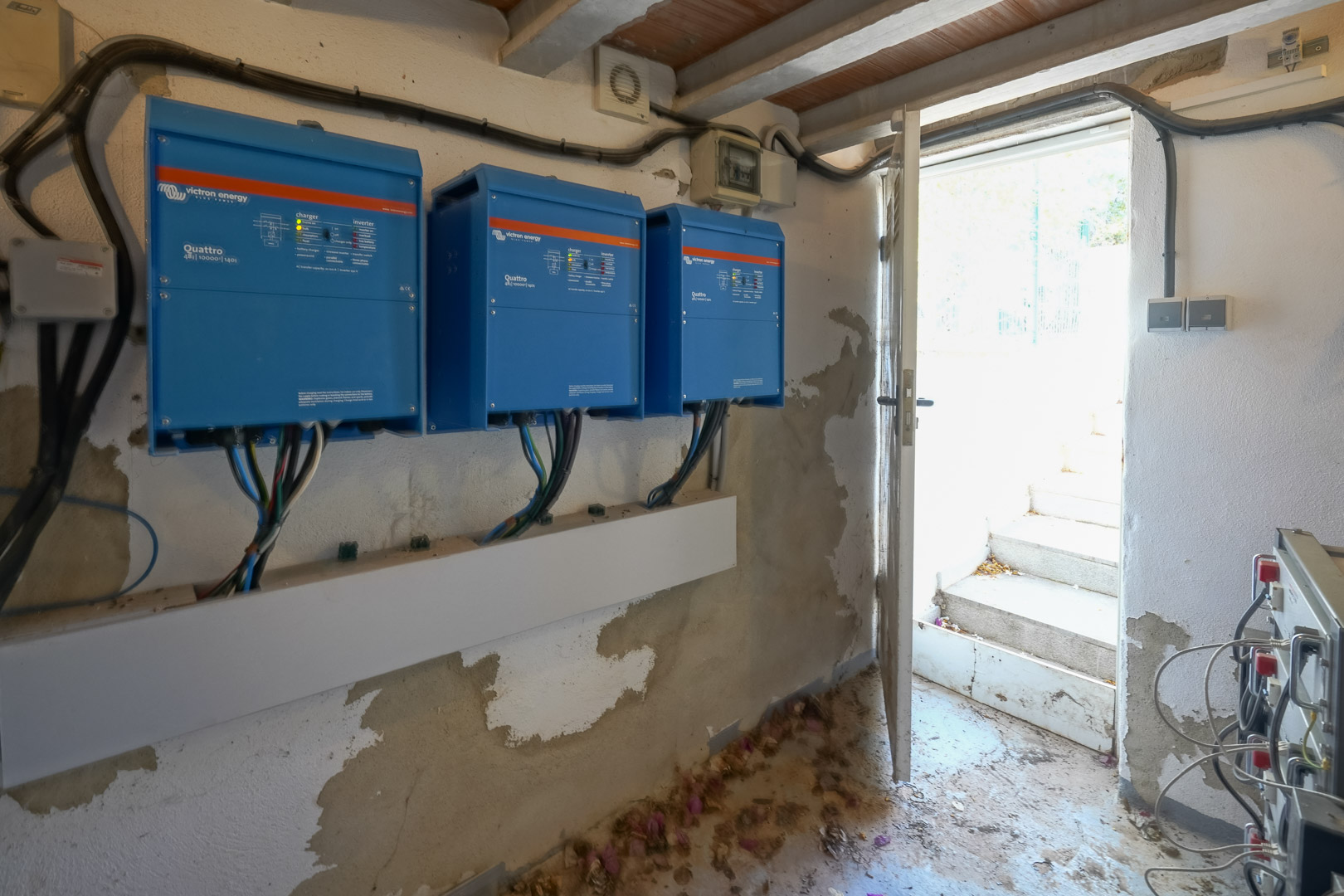 Technical room showcasing three Victron Energy Quattro inverters for the solar power system, situated by an open doorway to the outside.