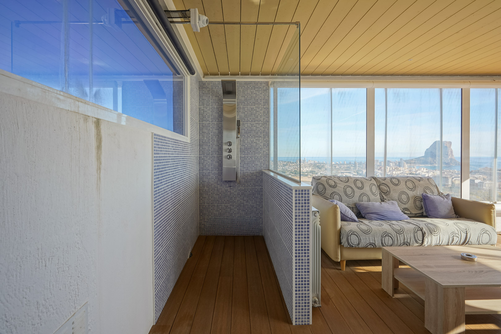 Upper-level wellness area featuring a hydromassage shower with blue mosaic tiles and a glass-enclosed lounge offering panoramic views of the Peñón de Ifach.
