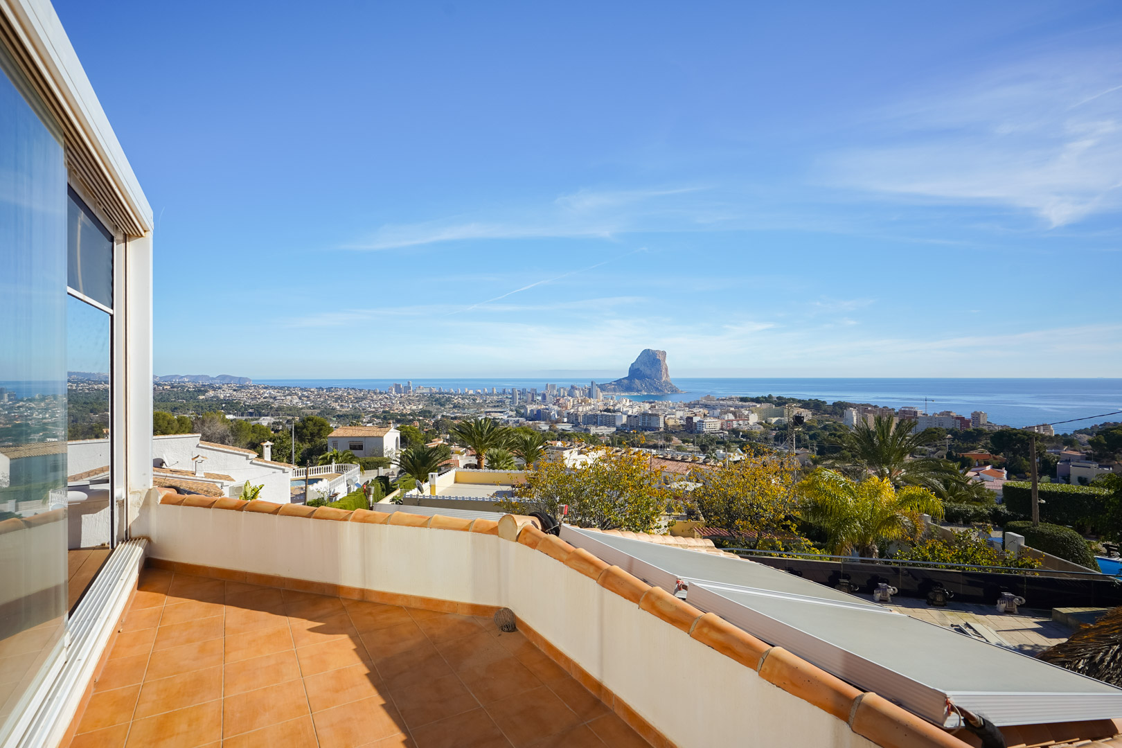 Upper terrace featuring terracotta tiling and panoramic views of the Peñón de Ifach and Calpe skyline. Solar panels are visible on the roof structure below.