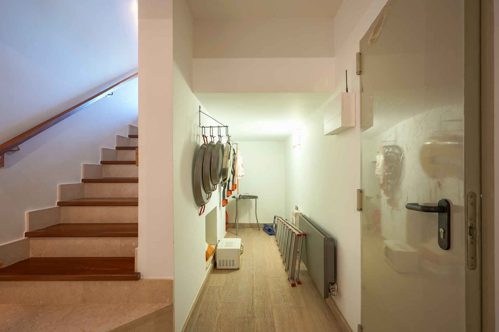 Utility hallway featuring storage for traditional cookware, situated next to a stone and wood staircase with a sleek handrail.