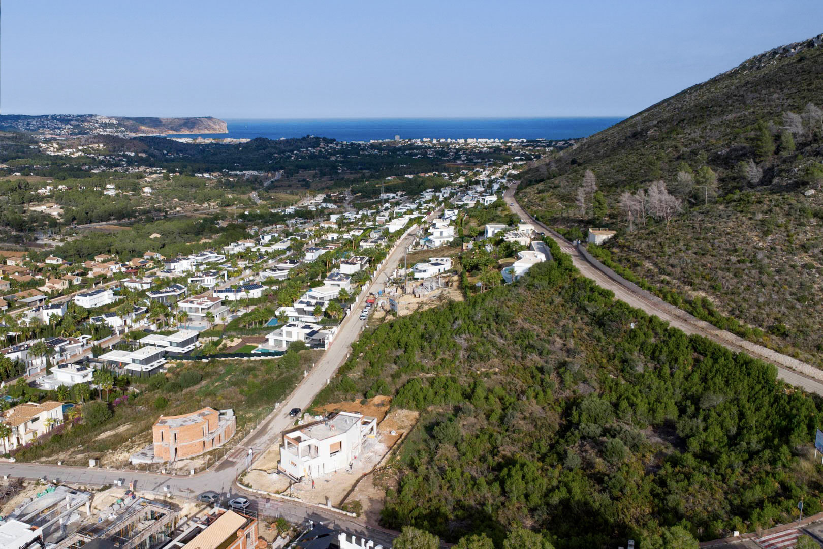 Aerial view of the building plot in Monte Olímpico, Jávea, overlooking a modern residential area with clear views of the Mediterranean Sea and Cabo de San Antonio.